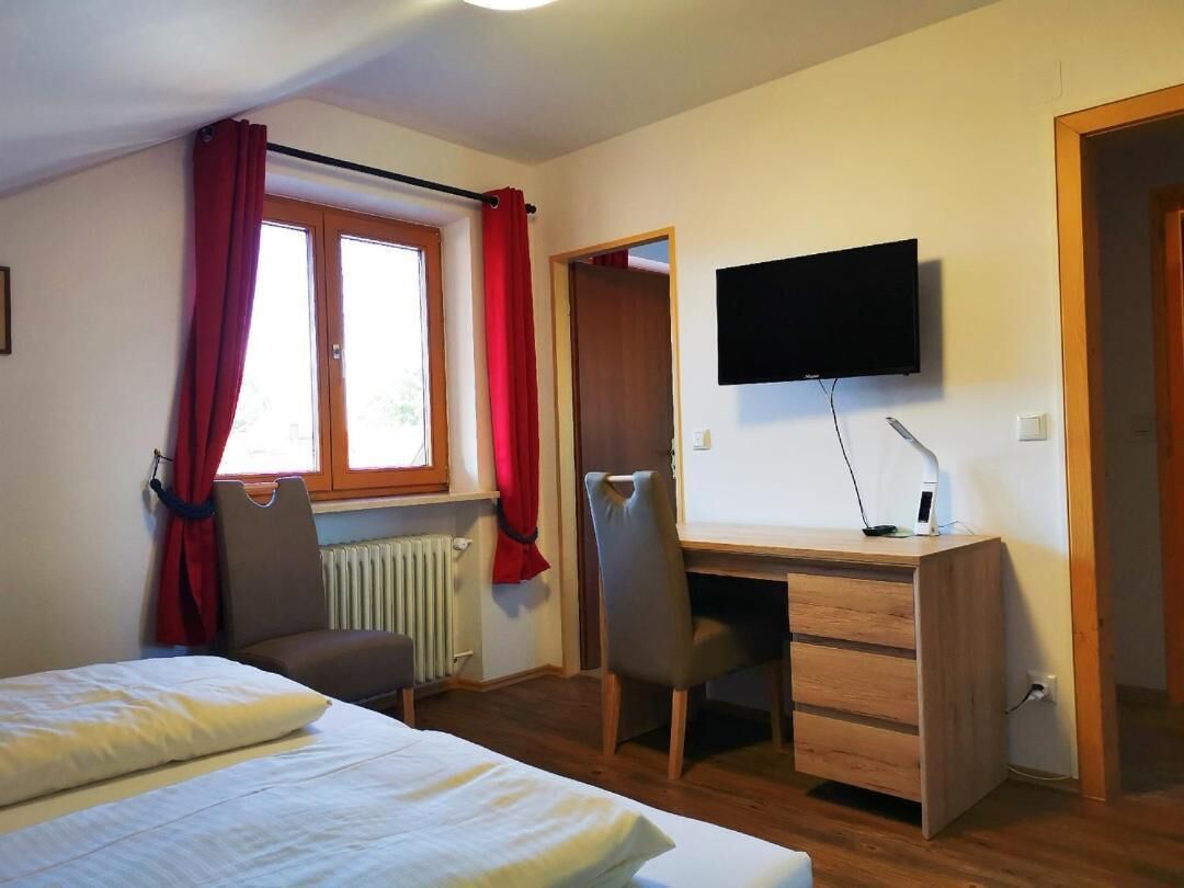 Ein Schlafzimmer mit einem Bett, einem Schreibtisch mit Computer, einem Stuhl und einem an der Wand befestigten Fernseher.