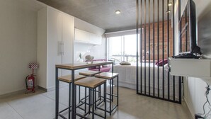 A modern kitchen with white cabinets, a wooden dining table, and a view of the city through large windows. - Soho Style Moderno Studio las Mercedes (Asunción)