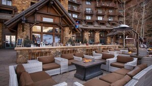 A lodge with a stone facade, outdoor seating area with wicker furniture, and a bar with a stone counter. - Bachelor Gulch Ritz-carlton 1 Bedroom Mountain Residence With Ski in, Ski out Access, Hot Tub, and Full Service Spa (Avon)