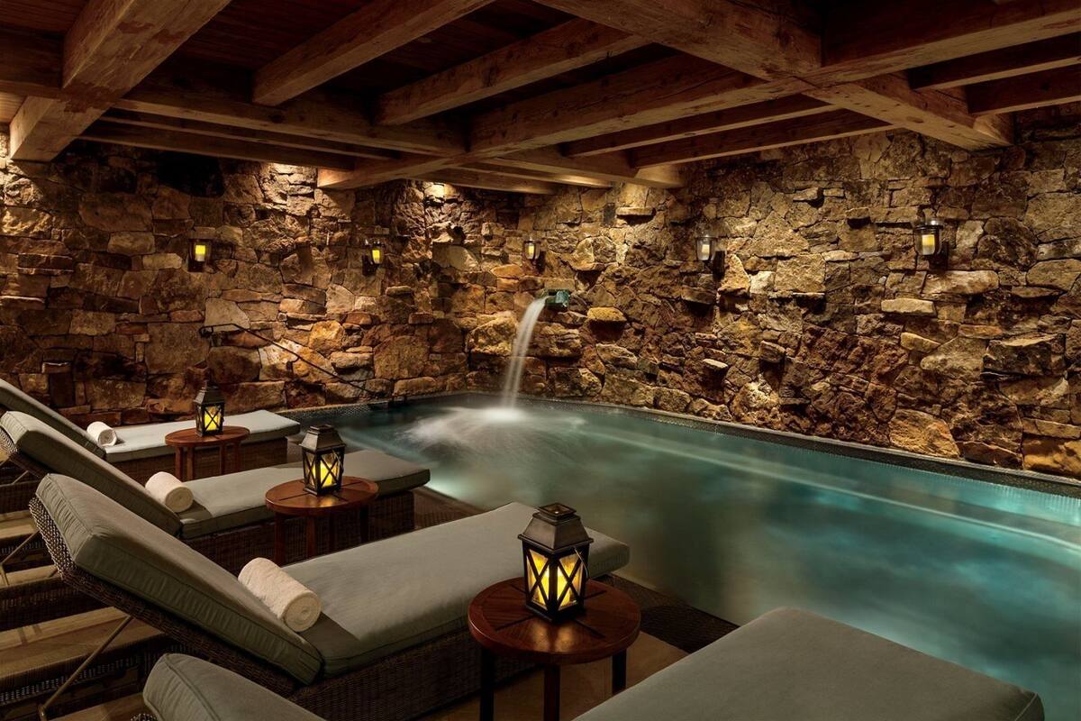 Un área de piscina interior con paredes de piedra, sillones de descanso y faroles.