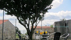An outdoor seating area with metal chairs and a table, two glasses of orange juice, and a tree providing shade. - Rustic house with sea views (Carnota)
