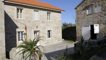 Un bâtiment en pierre avec un toit recouvert de tuiles rouges, un petit porche et une porte dotée d’un volet blanc.