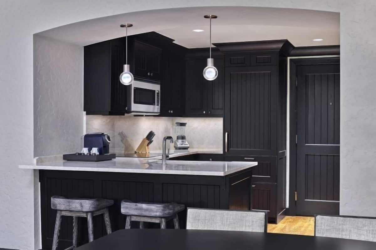 A modern kitchen with dark cabinetry, a central island with a sink, and pendant lighting.