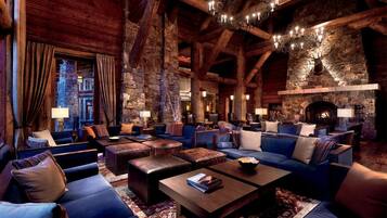 A log cabin interior with a stone fireplace, multiple seating areas, and a chandelier.