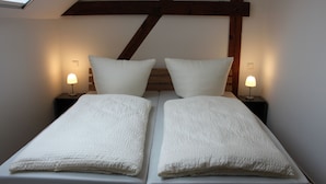 A twin bed with white bedding in a room with a sloped ceiling and exposed wooden beams. - Ferienwohnung Scheune (Lübbenau/Spreewald)