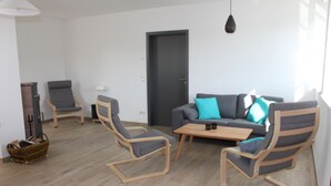 A modern living room with a grey sofa, two wooden rocking chairs, a coffee table, and a dark door. - Ferienwohnung Scheune (Lübbenau/Spreewald)