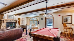 Une pièce chaleureuse avec une table de billard, une cheminée et une grande fenêtre donnant sur les arbres.