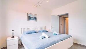 A bedroom with a bed, a nightstand, a wall-mounted picture, and a door leading to another room. - Apartment Casa Nova (Carvoeiro)