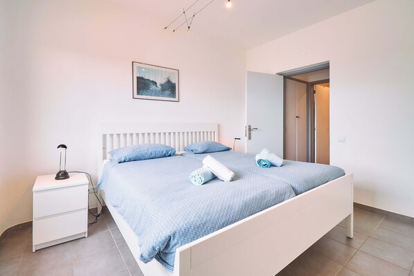 A bedroom with a bed, a nightstand, a wall-mounted picture, and a door leading to another room.