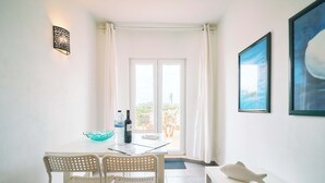 A room with a dining table, two chairs, a bench, a wall-mounted light fixture, and a framed picture. - Apartment Casa Nova (Carvoeiro)