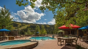 A pool area with lounge chairs and umbrellas, surrounded by a brick patio and trees. - 3 Bedroom Mountain Condo in River Run Village With Expansive Mountain Views and Walking Distance to Ski Slopes (Keystone)