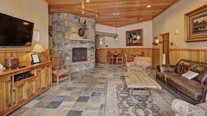 A cozy living room with a stone fireplace, wooden ceiling, and a large TV. - 3 Bedroom Mountain Condo in River Run Village With Expansive Mountain Views and Walking Distance to Ski Slopes (Keystone)