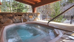 A hot tub with a stone wall backdrop, wooden deck, and a metal railing. - 3 Bedroom Mountain Condo in River Run Village With Expansive Mountain Views and Walking Distance to Ski Slopes (Keystone)