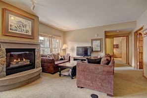 A cozy living room with a stone fireplace, comfortable seating, and a television. - 3 Bedroom Mountain Condo in River Run Village With Expansive Mountain Views and Walking Distance to Ski Slopes (Keystone)