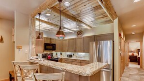 A kitchen with a central island, wooden cabinets, stainless steel appliances, and a rustic ceiling. - Ski In 3 Bedroom at Chateaux Dumont Keystone (Keystone)