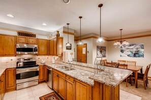 A kitchen with wooden cabinets, stainless steel appliances, granite countertops, pendant lighting, and a dining area with a table and chairs.