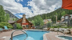 A pool area with a stone building, lounge chairs, and a mountain backdrop. - Private 3 Bedroom Townhome Located in East Keystone With Access to a Firepit, Hot Tub, and Billiards (Keystone)