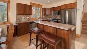 A kitchen with wooden cabinets, a stainless steel refrigerator, a microwave, and a stove. There are two stools and a window with a view of the outdoors. - Private 3 Bedroom Townhome Located in East Keystone With Access to a Firepit, Hot Tub, and Billiards (Keystone)