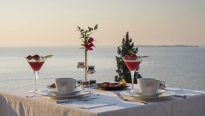 A table set for two with a view of the sea, two drinks, and a small plant. - Hotel Villa Rosenhof 1893 (Gardone Riviera)