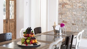 A dining table with a fruit centerpiece, white chairs, and a stone wall in the background. - Hotel Villa Rosenhof 1893 (Gardone Riviera)