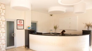 Balcão de recepção de hotel com recepcionista, placa de proibido fumar e um letreiro de boas-vindas emoldurado.