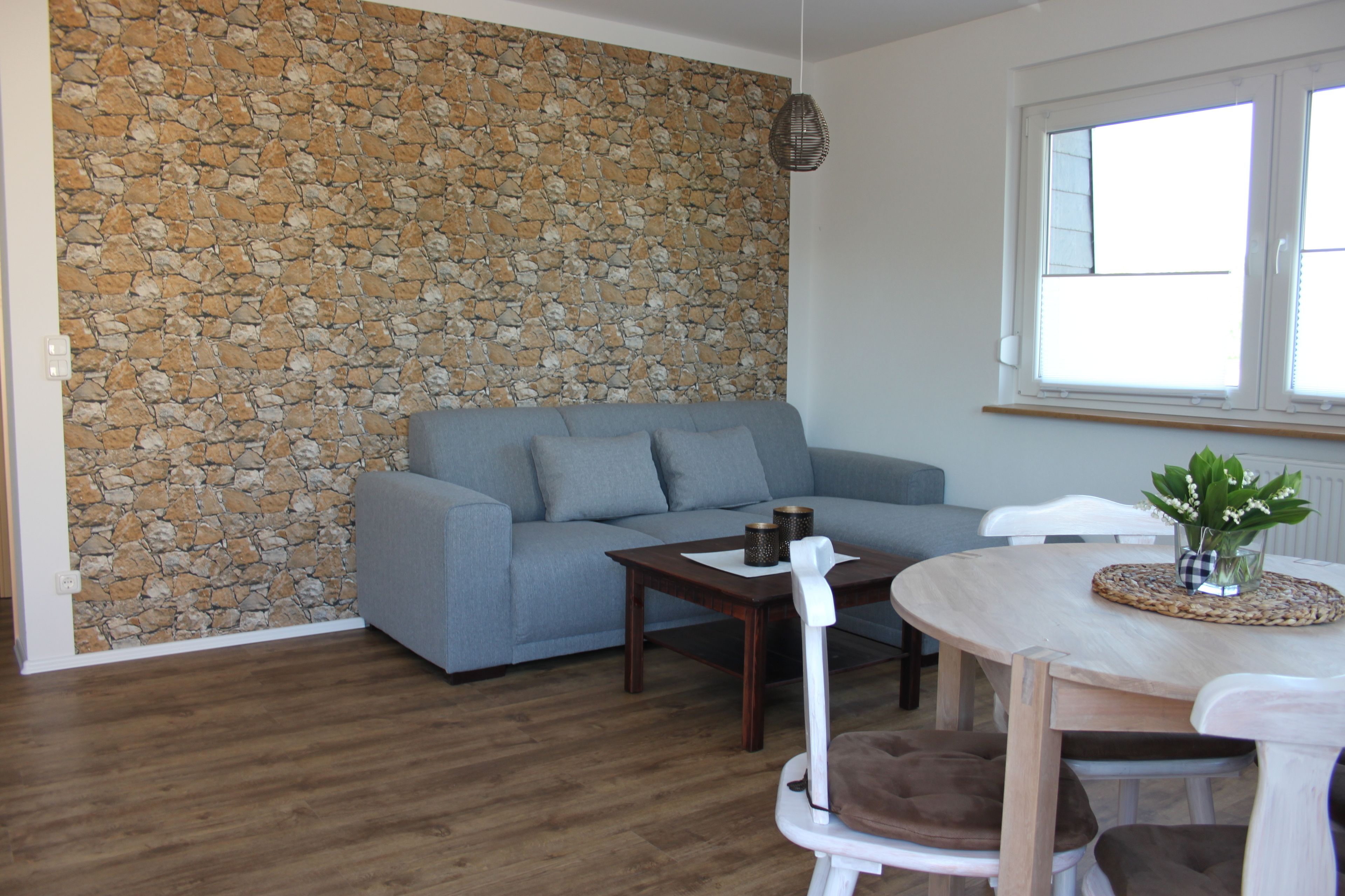 A living room with a stone wall, a grey sofa, a wooden coffee table, and a white chair.