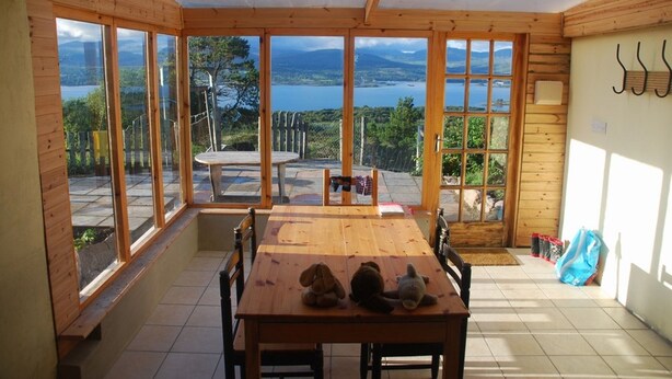 A wooden interior with large windows offering a scenic view of a lake and mountains. - Beara jewel, Simple but complete appartment style property with stunning view. (Kenmare)