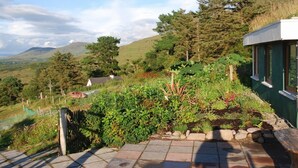 A garden with a stone pathway leading to a bench, surrounded by various plants and trees. - Beara jewel, Simple but complete appartment style property with stunning view. (Kenmare)
