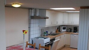 A compact kitchen with white cabinets, a microwave, a stove, and a dishwasher. There is a dining table with chairs and a vase with flowers. - Beara jewel, Simple but complete appartment style property with stunning view. (Kenmare)