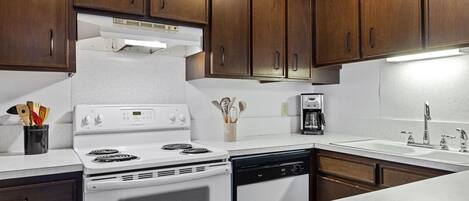 A kitchen with wooden cabinets, a white stove, a dishwasher, and a coffee maker.