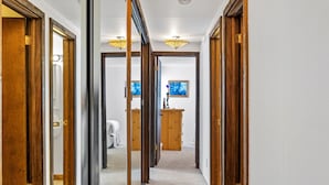 Un pasillo con puertas de madera y una vista a una habitación con un aparador de madera y un cuadro en la pared.