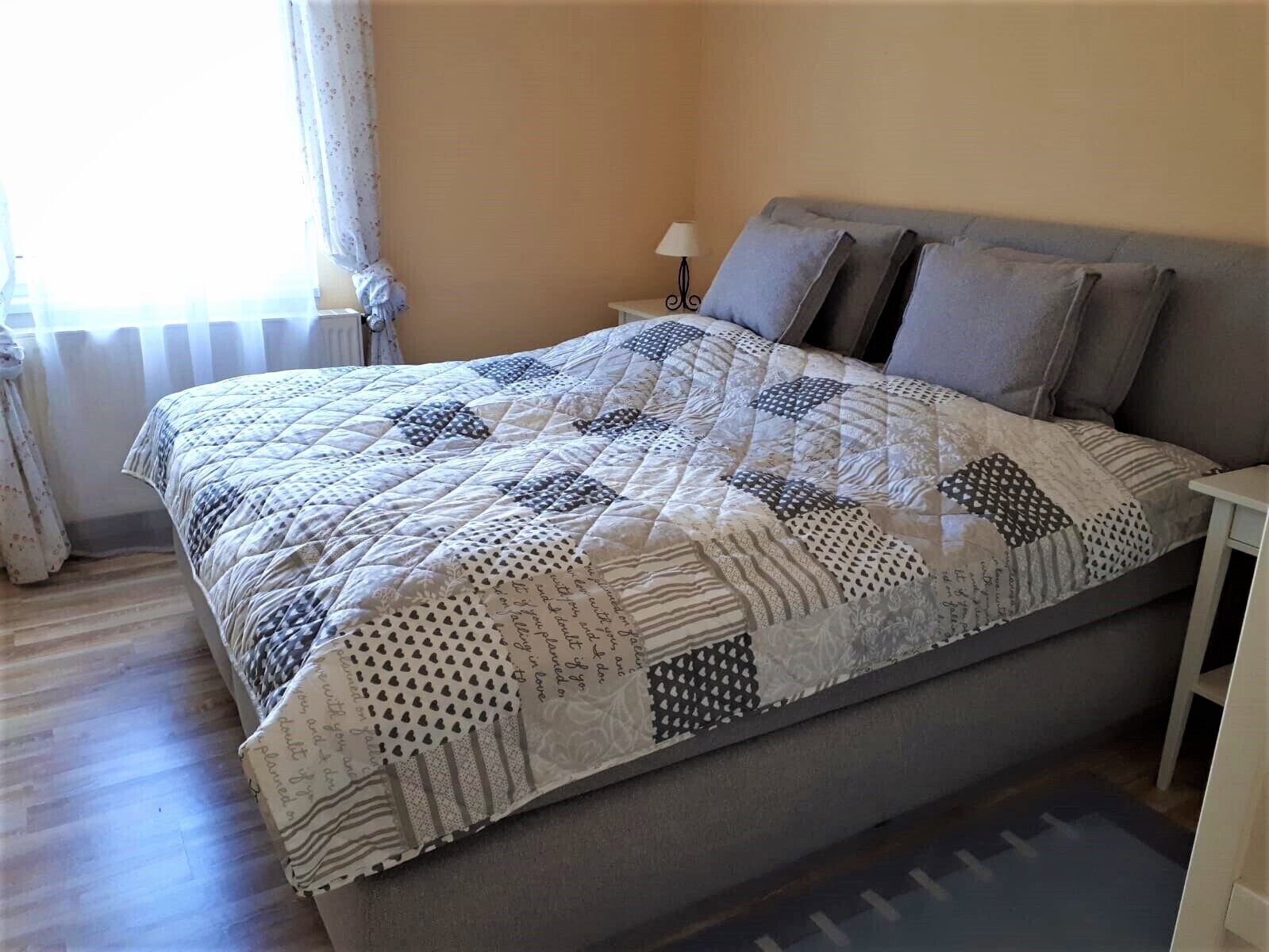 A neatly made bed with a patterned quilt, a bedside lamp, and a window with curtains.