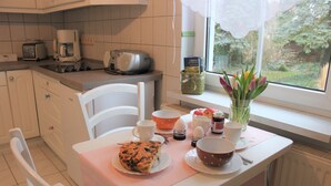 A kitchen with a dining table set for two, a toaster, a coffee maker, and a window with a view of greenery.