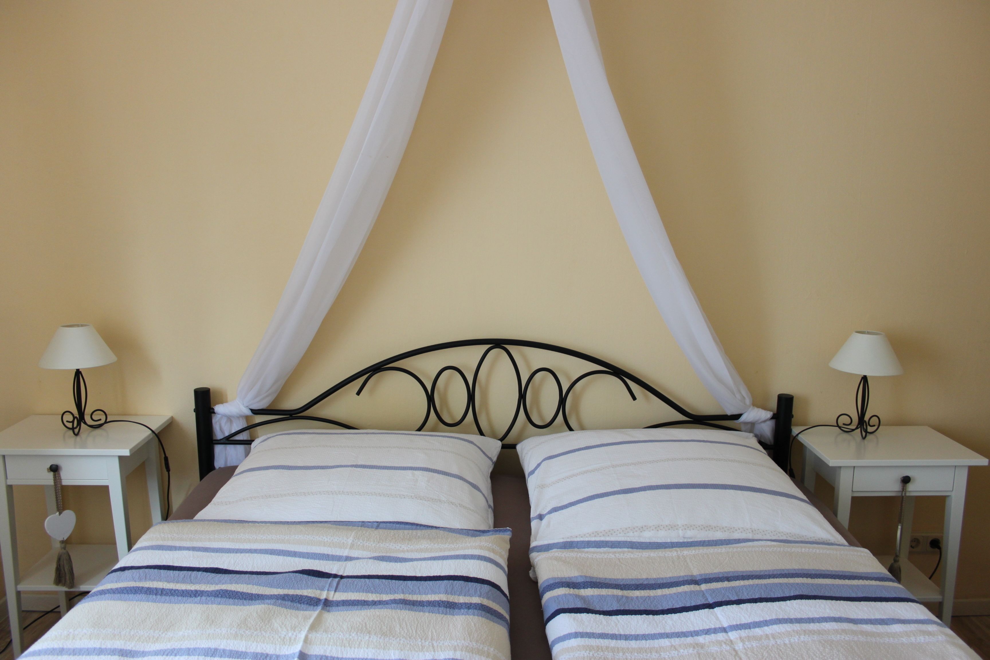 A double bed with a canopy, two bedside tables with lamps, and a neutral-colored wall.