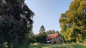 A traditional brick building with a red roof, surrounded by lush greenery and a clear sky.