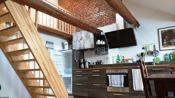 A kitchen with a wooden staircase, a brick wall, and a flat-screen TV mounted above the counter.