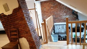 A loft-style room with exposed brick walls, wooden flooring, and a staircase leading to an upper level.