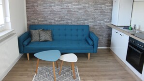 Une cuisine moderne avec un canapé bleu, deux petites tables et un mur décoré d’un motif en briques.