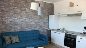 Une cuisine moderne avec des meubles blancs, un canapé bleu et un coin repas avec deux chaises.