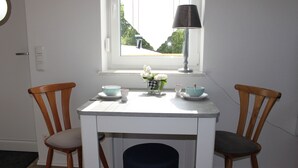 Un coin repas avec une table blanche, deux chaises en bois, un petit vase avec des fleurs et une lampe.