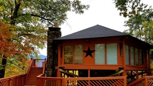 A wooden cabin with a stone chimney, a star decoration, and a staircase leading to a deck. - Mountain View/2 King Suites/Hot Tub/Pool Table/Minutes to Ober & Downtown (Gatlinburg)