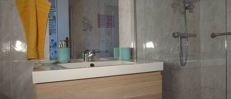 A bathroom with a white sink, wooden vanity, a glass shower enclosure, and a yellow towel on a hook.