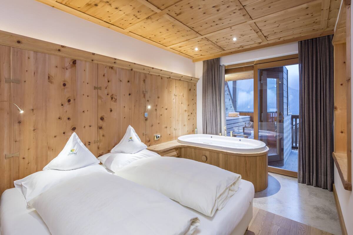 Une chambre à coucher aux murs lambrissés, dotée d’un grand lit, d’une baignoire et d’un balcon avec vue.