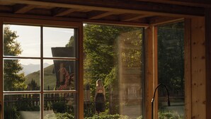 A modern interior with a large window, wooden ceiling beams, and a sofa. - Naturhotel Lüsnerhof (Luson)