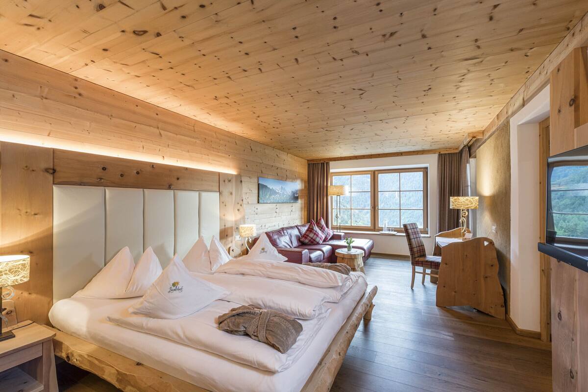 Une pièce aux murs lambrissés, comprenant un grand lit, un canapé, un fauteuil et un bureau.