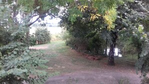 A pathway surrounded by dense foliage and trees, leading to a body of water. - Country home (Roquefort)