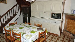 A dining area with a table set for four, wooden chairs, a staircase, and a kitchen area with cabinets and a microwave. - Country home (Roquefort)
