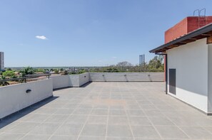 A rooftop terrace with a clear view of the cityscape, featuring a modern building with a red roof and a white wall.