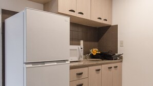 Eine moderne Küche mit hellen Holzschränken, einem weißen Kühlschrank, einer Mikrowelle und einer kleinen Arbeitsfläche mit einer Blumenvase.