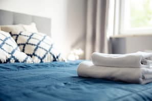 A neatly made bed with blue bedding and white towels, a checkered pillow, and a window with curtains. - Business Mokotow Park 214 Apartment (Warsaw)